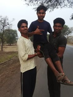 three young men standing on the side of a road with one holding onto another man's leg