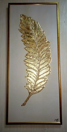 a gold leaf is hanging on the wall in front of a white background with a golden frame