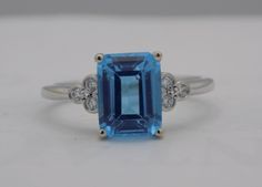 A 14k white gold ring holds this 2.70 carat, emerald cut, blue topaz center stone. Six bezel set accent diamonds (three to each side of the topaz) frame the topaz for .08 diamond ctw. The ring is now a size 7. 14k White Gold Ring, Emerald Cut, Bezel Setting, White Gold Rings, Blue Topaz, Sapphire Ring, Emerald, Topaz, Diamond Ring