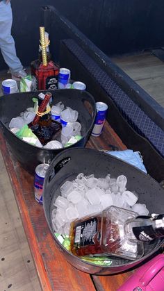 two buckets filled with ice and drinks on top of a wooden table next to another container