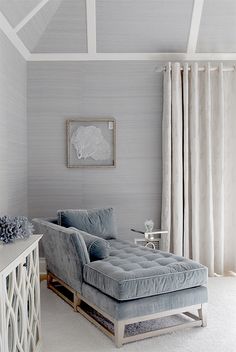 a blue chaise lounge in a white room with curtains and drapes on the windows