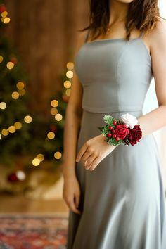 a woman wearing a gray dress and holding a red rose in her left hand with christmas lights behind her