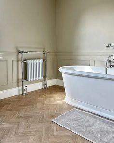 a bathroom with a bathtub, towel rack and rug on the floor in front of it