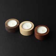 three wooden candles sitting next to each other on a black surface with one lit candle in the middle