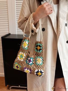 a woman in a trench coat is holding a handbag with beads and flowers on it