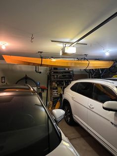 two cars are parked in a garage with an overhead kayak attached to the ceiling