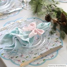 a table set for christmas dinner with place settings and pine cones on the table top