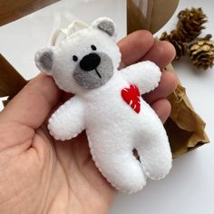 a small white teddy bear with a red heart on it's chest sitting in someones hand