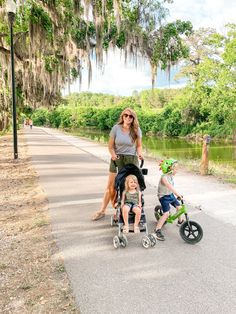 a woman and two children are walking down the street with their dog on a tricycle