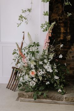 an arrangement of flowers and greenery in front of a fireplace