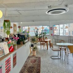 a room filled with lots of tables and chairs next to a counter topped with potted plants