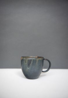 a black cup sitting on top of a white table next to a gray wall and floor