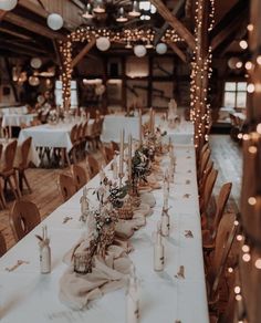 a long table with candles and flowers on it in a room filled with wooden chairs