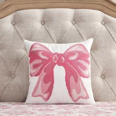 a pink bow pillow sitting on top of a white bed next to a beige headboard