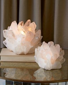 two crystal sculptures sitting on top of a wooden table next to a book and window