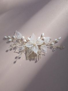 a bridal hair comb with flowers and leaves on the side, against a pale background