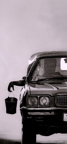 a black and white photo of a car with its hood up, holding a bucket