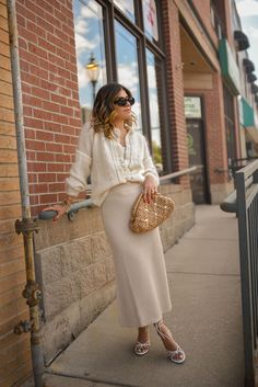 Need a casual chic outfit to wear this summer? CHIC TALK is sharing how she has been wearing this knit midi skirt on repeat this summer. She pairs cream cardigan with a knit skirt and a rattan clutch bag for this chic date night outfit. Visit the blog for more outfit inspiration, summer fashion trends, and 2024 style guides. Long Knitted Skirt Outfit, Cream Knit Skirt Outfit, Tan Skirt Outfit, Tan Skirt Outfits, Cream Skirt Outfit, Cream Silk Skirt, Sunday Attire, Midi Skirt Outfit Winter