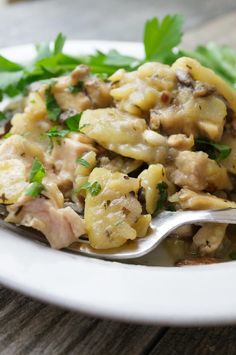 a white plate topped with pasta covered in meat and parsley next to a fork