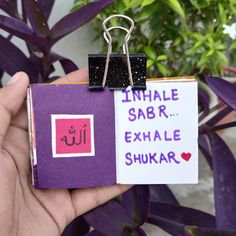 a hand holding a small purple and white book with the word inhale saar exhale shukar written on it