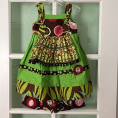 a green and brown dress hanging on a white door with an open window behind it