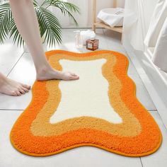 a person is standing on the bathroom floor with an orange and white rug in front of them