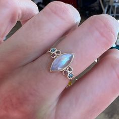 This incredible Marquis Moonstone is set between clusters of vibrant Blue Zircons and Warm Peach Sapphires. Finished with Emily's handmade Seagrass band we love it as an alternative engagement ring or right hand ring. Approximate stone size: 12mm x 6mm 2.3cts Mohs Stone Hardness: 6-6.5 This one of a kind piece is handmade to order in Emily's Hudson Valley studio. If you have questions about sizing, shipping or custom orders please reach out to us! Marquise Rose Cut Diamond Jewelry For Promise, Fine Jewelry Marquise Multi-stone Cluster Ring, Marquise Multi-stone Cluster Ring Fine Jewelry, Marquise Cut Multi-stone Cluster Ring For Anniversary, Anniversary Marquise Cut Multi-stone Cluster Ring, Marquise Multi-stone Cluster Ring For Anniversary, Multi-stone Sapphire Rings Marquise Cut, Yellow Gold Multi-stone Moonstone Jewelry, Heirloom Yellow Gold Multi-stone Moonstone Ring