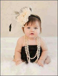 a baby girl wearing pearls and a headband with feathers on it's head