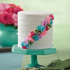 there is a white cake with flowers on it and two green vases in the background