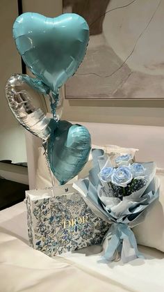 a bouquet of blue roses and balloons on a bed next to a gift box with a heart shaped balloon