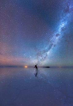 a person standing in the middle of a body of water under a night sky filled with stars