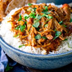 a blue bowl filled with rice and meat on top of a wooden table next to bread