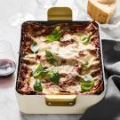 a casserole dish on a table with bread and wine