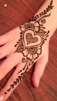 a henna tattoo on someone's hand that is decorated with hearts and leaves