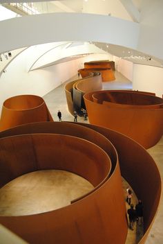 the inside of a building with lots of round wooden benches and people standing in it