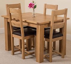 a wooden table with four chairs and a flower vase on top of it in front of a white wall