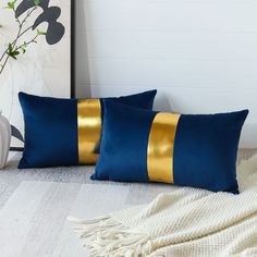 two blue and gold pillows sitting on top of a white rug next to a vase