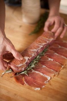 a person cutting up meat on top of a wooden table with rosemary sprigs