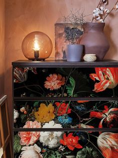 a dresser with flowers painted on it next to a lamp