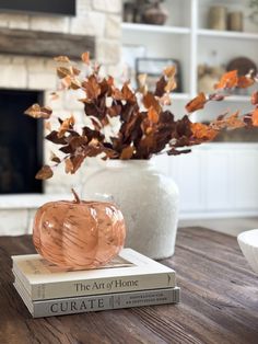 two books sitting on top of each other next to a vase with leaves in it