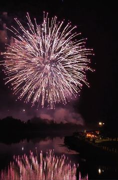 fireworks are lit up in the night sky over a body of water with reflections on it