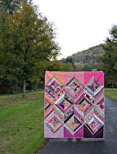 a patchwork quilt is displayed on the side of a road in front of some trees