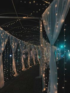 a walkway covered in white sheer curtains and fairy lights