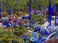 blue and white glass sculptures are in the middle of a flower garden with purple flowers