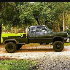 a green pick up truck parked on top of a dirt road in front of trees