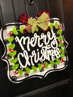 a merry christmas sign hanging on the front door with holly wreaths and plaid bow