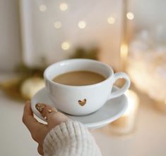 a woman holding a cup of coffee in her hand with gold hearts on the saucer