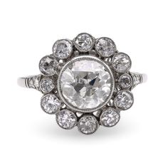 Center Stone: Diamond Cut: Old European Cut Weight: 1.25 Carat Color: L Clarity: SI Accent Stone: 16 Diamonds Cut: Single, Old European, Old Mine and Round Brilliant Cuts Weight: Approximately 1.5 Carats Color: I Clarity: SI Metal: Platinum Era: Modern Circa: 2020's in the Style of Art Deco Hallmarks: Stone Weight Engraved Size: 7.5 and can be resized Gram weight: 4.68 This striking ring, designed in the style of Art Deco from the 2020s, showcases a captivating 1.25-carat old European cut diamon Luxury Platinum Cluster Halo Ring, Luxury Cluster Halo Ring In Platinum, Gia Certified Platinum Cluster Diamond Ring, Luxury Platinum Cluster Ring With Rose Cut Diamonds, Platinum Cluster Ring With Rose Cut Diamonds, Colored Stone Engagement Rings, Yellow Gold Cocktail Ring, Unique Rings Vintage, Platinum Diamond Engagement Rings