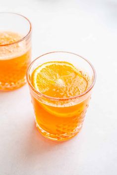 two glasses filled with orange juice sitting on top of a white table next to each other