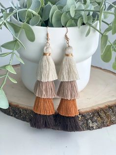 two tone tasselled earrings with gold and brown accents on top of a tree stump